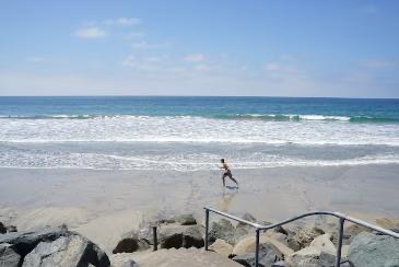 A quiet stretch of St. Malo beach with a lone surfer at the waterline