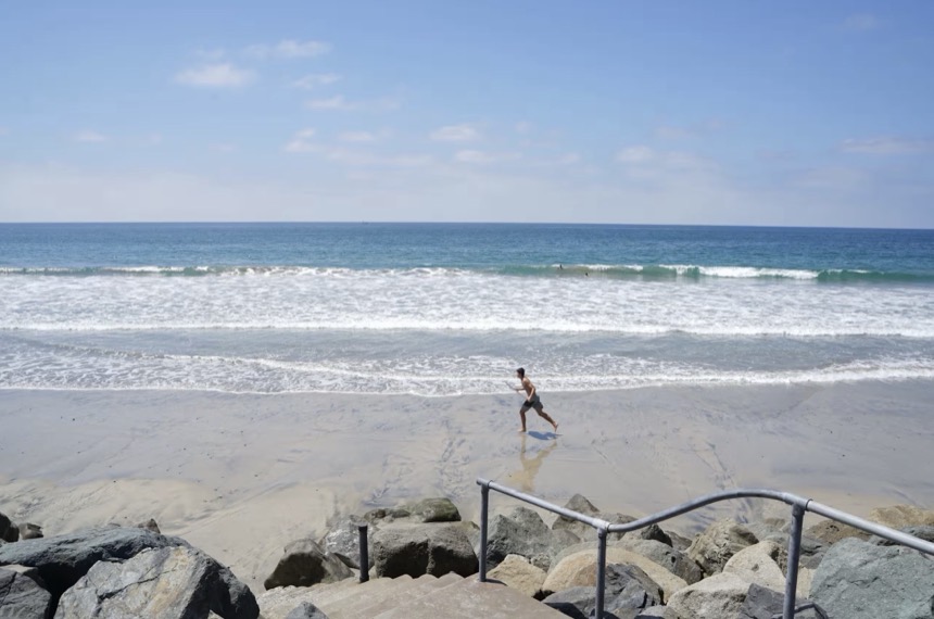A quiet stretch of St. Malo beach with a lone surfer at the waterline
