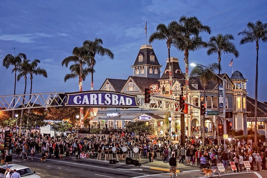 The Carlsbad Village sign lit at dusk above a crowded street